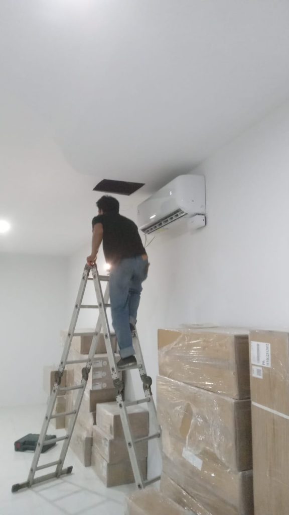 Teknisi di dekat unit AC indoor pada tangga kerja